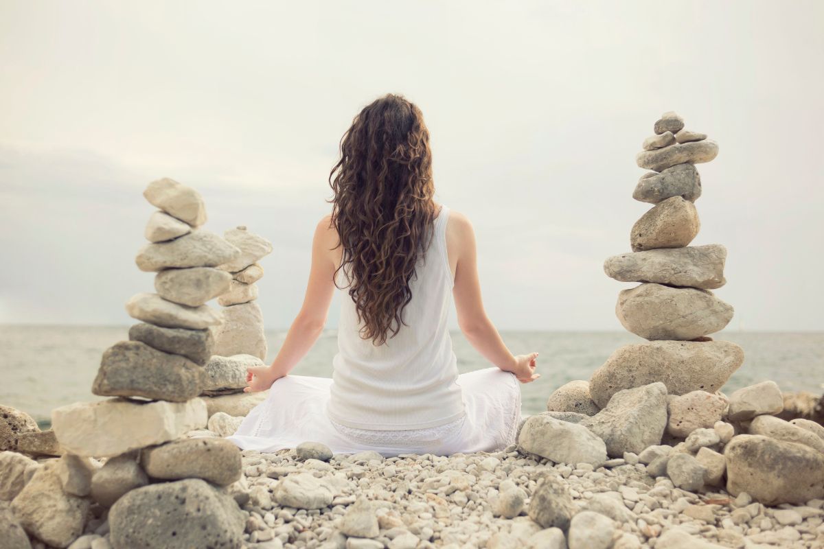 Woman with ADHD finds balance by sitting peacefully and meditating next to the ocean.